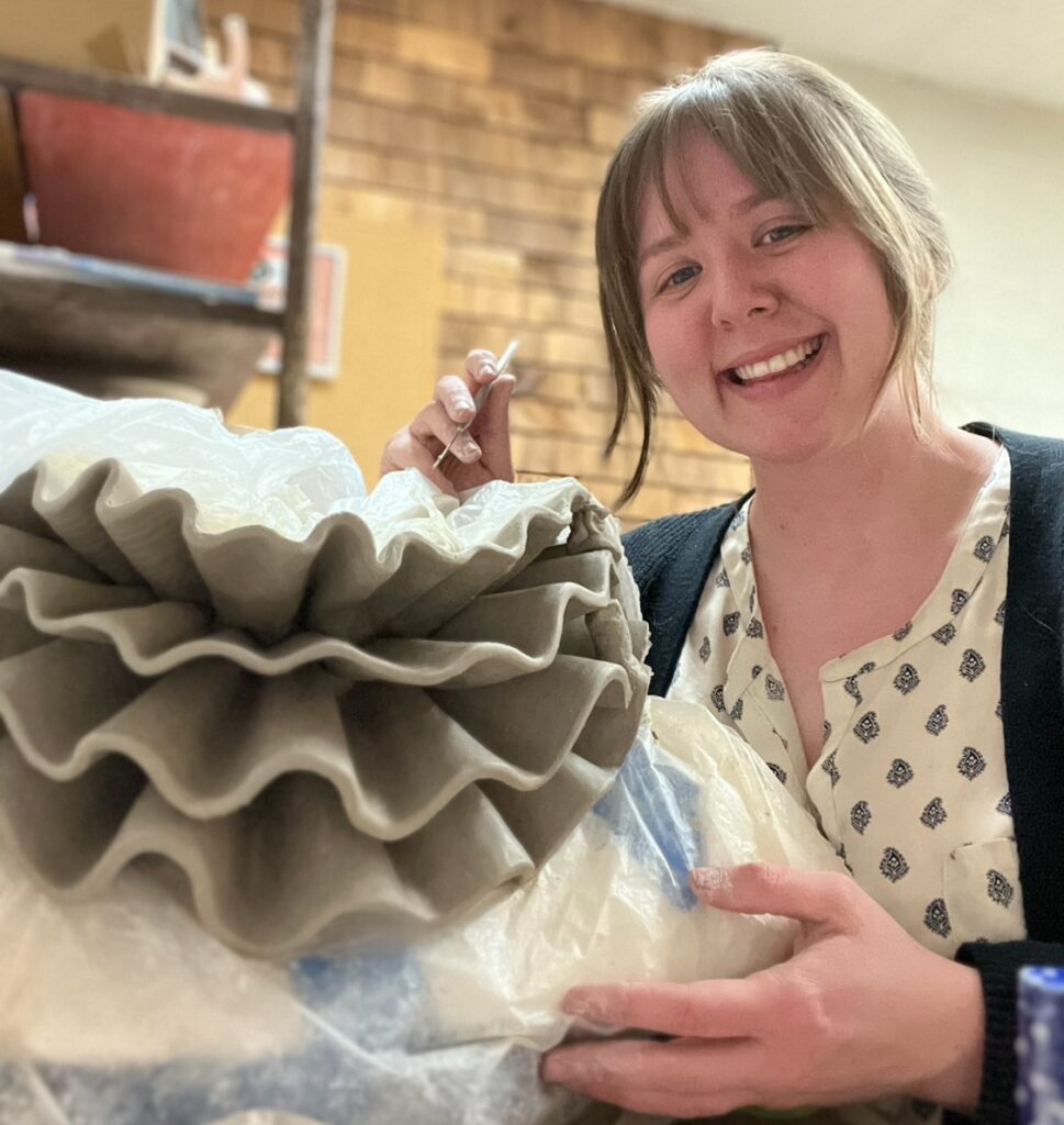 Woman smiling while working on a ceramic collar in her studio.